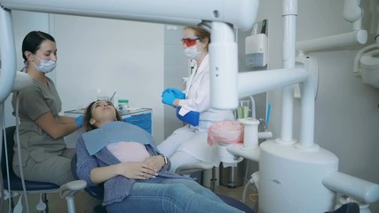 The start of dental treatment, doctor lower the dental chair. Dentist turn on the lamp, female open the mouth.