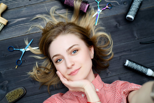 Selfie photo of  happy smiling young woman in plaid shirt with hairdresser tools among her