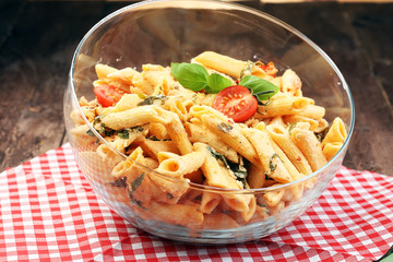 Penne pasta in tomato sauce with chicken, tomatoes decorated with basil on a wooden table