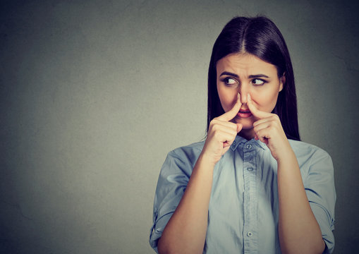 Woman pinches nose with fingers looks with disgust sideway something stinks bad smell