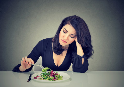 Displeased young woman eating green leaf lettuce tired of diet restrictions