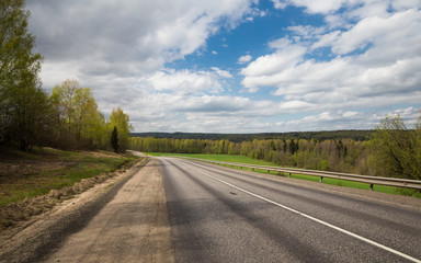 A Deserted country road along the forest under blue sky with clouds