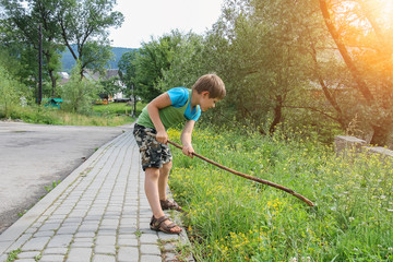 Boy playing with wooden stick on roadside in sunlight