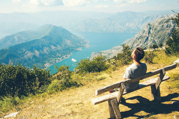 Fototapeta na wymiar The guy in the mountains in the background Bay in Montenegro. A guy sits on a bench in the mountains in Kotor Bay