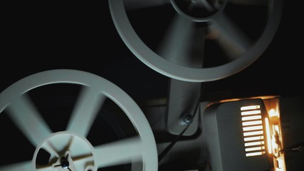 Old 8mm film projector playing in the night. Close-up of a reel with a film.