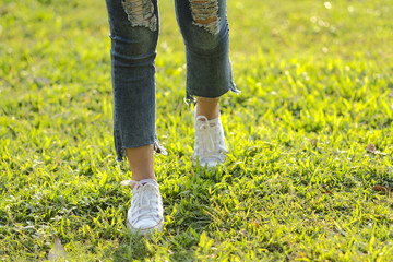 woman wear sneaker jeans walking on grass with sunlight
