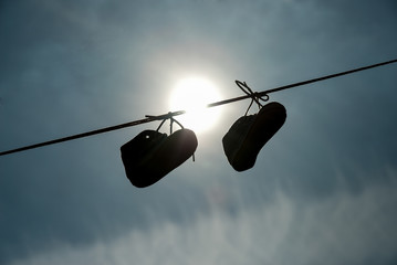 New-born child shoes hanging on the lace with clear sky and sun in background