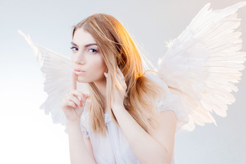 Angel keeps the secret. Young, wonderful blonde girl in the image of an angel with white wings.