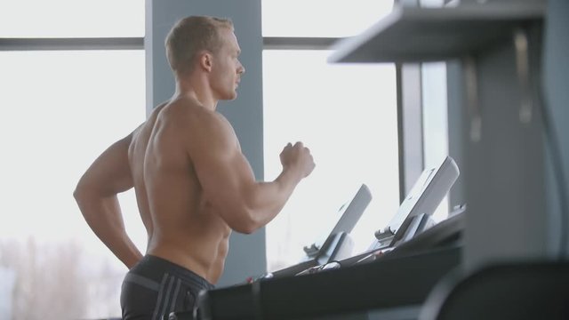 Muscular man running on a treadmill in the gym