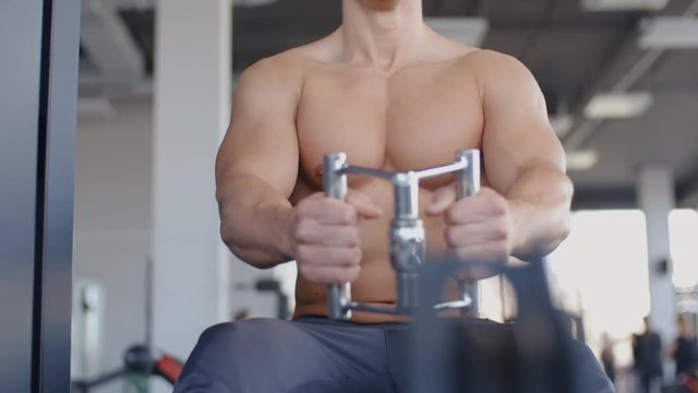 Muscular sportsman pulling down cable of crossover machine and doing exercise in the gym