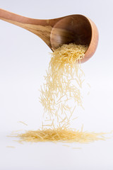 Raw pasta filini on a white background, falling from a wooden spoon.
