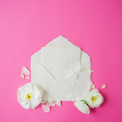 White flowers, petals and paper envelope on pink background. Flat lay, top view. Vintage background.