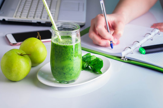 Freelancer Woman right hand writing on notebook and laptop, mobile smart phone nearby.Healthy Drink Smoothie from Green Spinach