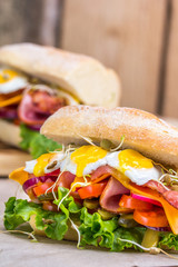 A sandwich with bacon, cheese and fried quail eggs. A sandwich with fresh vegetables and herbs on a wooden background.