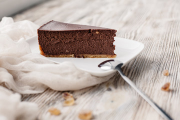 A slice of a chocolate cheese cake on a wooden background with some cane sugar cubes around. Low depth.