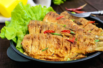 Fried fish carp (sazan) on a cast-iron frying pan with lettuce leaves on a dark wooden background. Close up