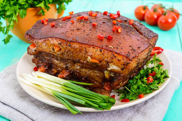 A large piece of baked bacon with spices, green onions on a plate.