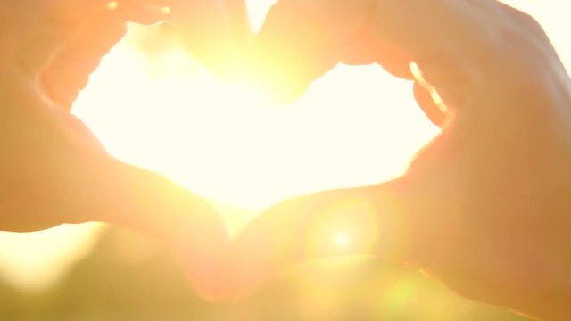 Person making heart with hands over nature sunset background. Silhouette hand in heart shape with sun inside. 4K UHD video 3840X2160
