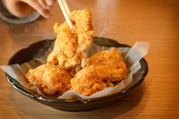 Warm tone with fried chicken and chopsticks in black dish on the wooden table.