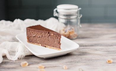 Кусок торта чизкейка на тарелке, деревянный фон. A slice of a chocolate cheese cake on a wooden background with some cane sugar cubes around. Low depth. 