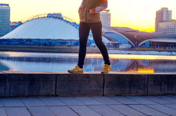 Young woman walking along the embankment in the city at sunset time. Hurry up concept