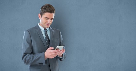 Businessman texting on smart phone against wall