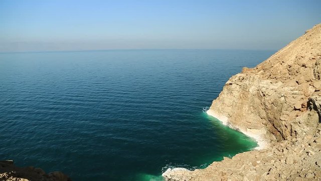 Rocky shore of Dead Sea in Hashemite Kingdom of Jordan. Green water and white salt deposits on yellow rocks