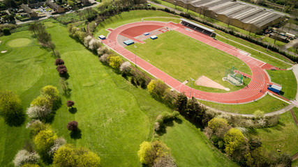 Track and field. Aerial view of athletes training on a North London running track set by a golf course on a bright sunny day. - 146474312