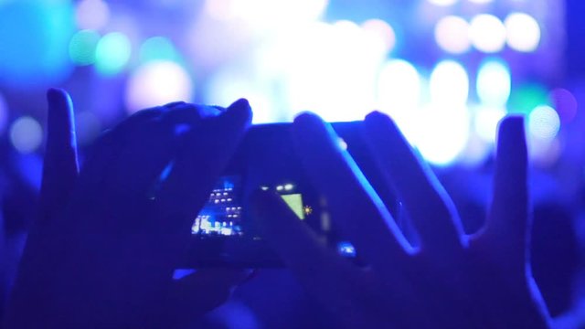 Close-up of hands focusing mobile phone camera on stage, filming concert video