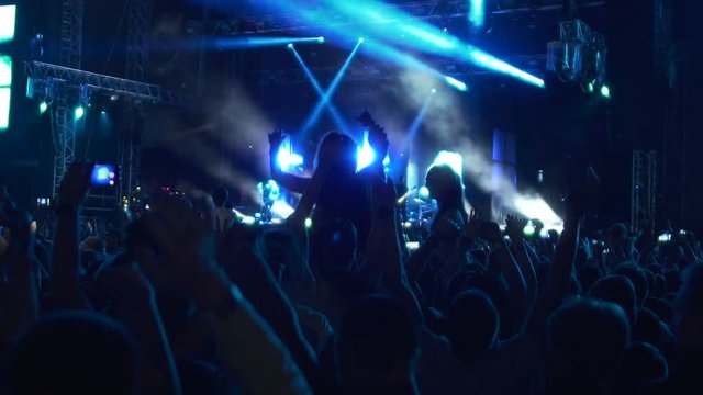 Crowd of excited people dancing at concert of beloved music band, slowmo