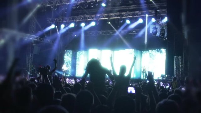 Crowd of music fans dancing under luminous rays of LED illumination, concert