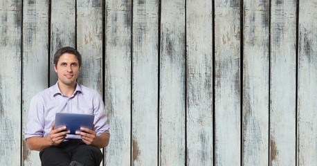 Businessman holding digital tablet against wooden wall