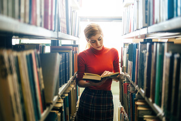 Portrait of college girl reading book in library