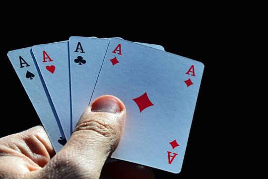 Four aces from canasta joker from 52 card French deck held in male left hand on dark background