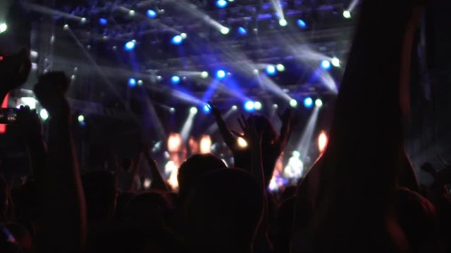 Silhouettes of fans waving hands in brightly illuminated concert hall, dancing