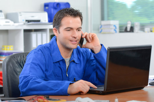 Man in overalls on laptop and talking on telephone