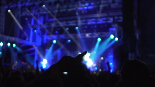 Excited music fans dancing at concert in shimmering lights, waving hands