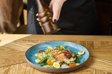 Vegetable salad with cucumber, lettuce, cherry tomatoes, salmon and eggs. Woman waitress pepper dish