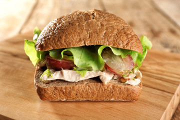 Wooden board with chicken salad in burger bun on table