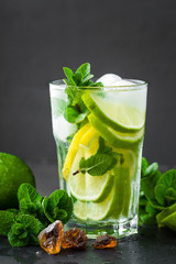 Refreshing mint cocktail mojito with rum and lime, cold drink or beverage with ice on black background