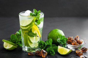 Refreshing mint cocktail mojito with rum and lime, cold drink or beverage with ice on black background