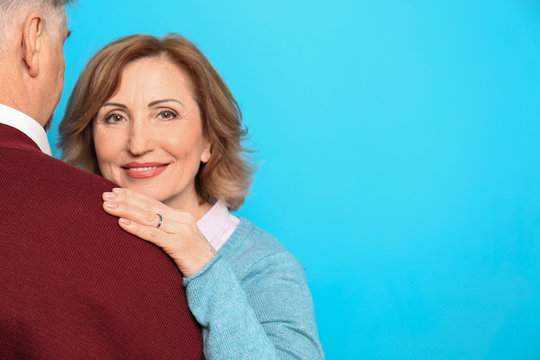 Happy senior woman embracing her husband on color background