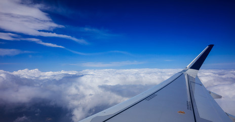 Fototapeta na wymiar Plane wing over clouds on a blue sky background