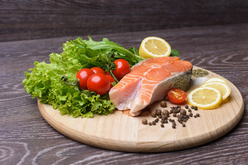 Raw salmon steaks on the wooden board. Lettuce leaves, spices, lemon slices on a wooden board. Woody background.