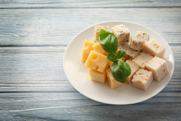 Plate with different tasty cheese on wooden table