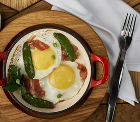 bacon and eggs with green peas in red pan served on wooden table in restaurant