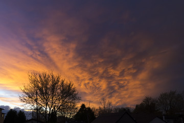 Fototapeta na wymiar Dramatic sunset sky reflecting off of storm clouds approaching neighborhood in silhouette