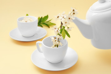 Pouring fruit tree branch from teapot into cup on color background