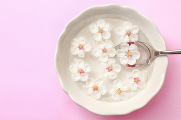 Bowl with fruit tree flowers, water and spoon on pink background