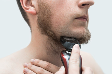 young man shaving his beard off with an electric shaver. Three-quarter view